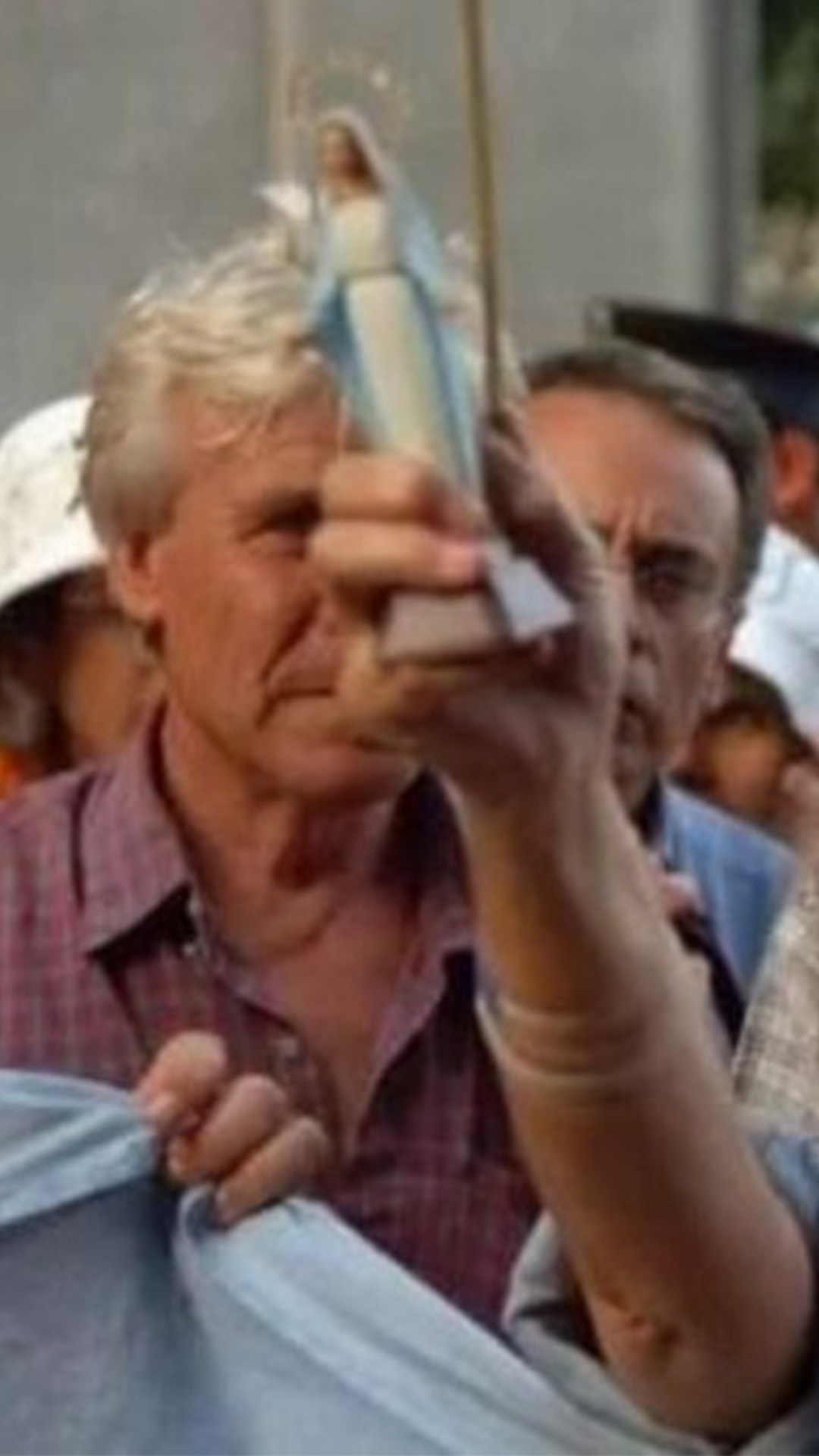 Cacerolazos en la calle. En primer plano una mujer alza una estatuilla de una Virgen y en la otra tiene una cacerola con una cuchara.