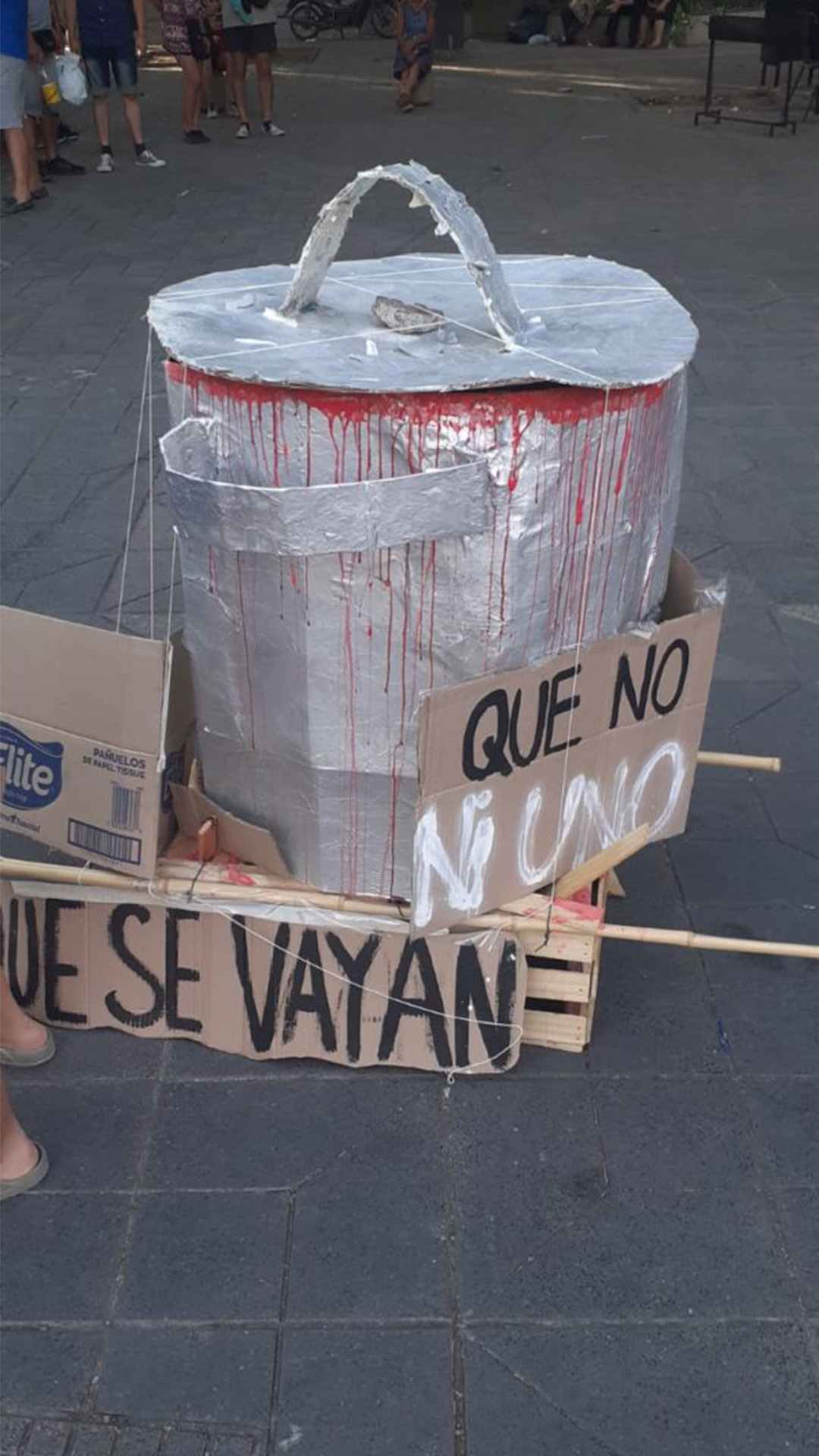 En el medio de la calle una cacerola echa de cartón, manchada de pintura roja que simula sangre. Sobre el costado de la misma se puede leer un cartel que dice que se vayan.