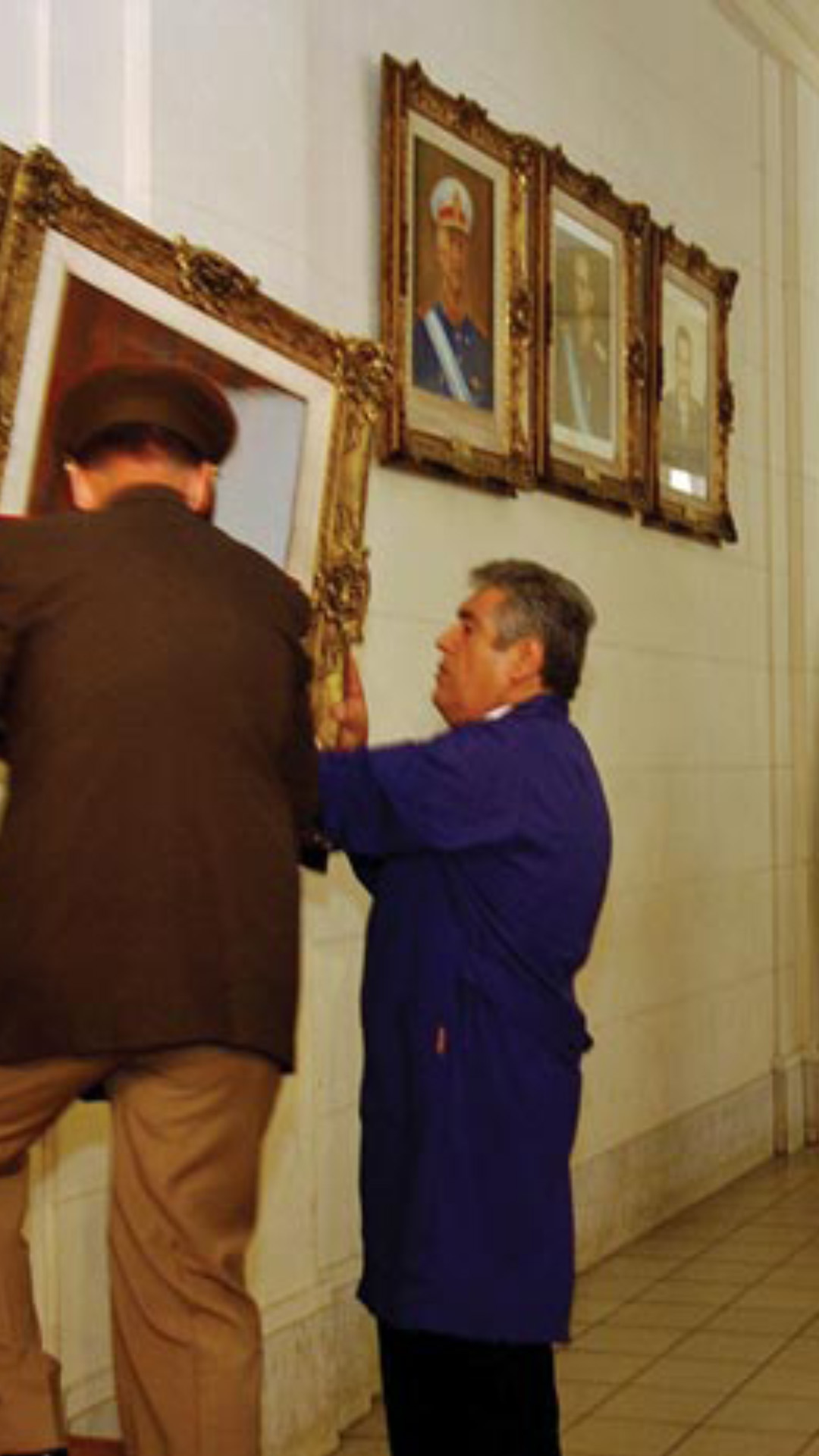 Nestor Kirchner, presidente en 2004, mirando como personal de las fuerzas armadas y personal de mantenimiento descuelgan el cuadro del presidente de facto Rafael Videla. En el fondo personal de seguridad.
