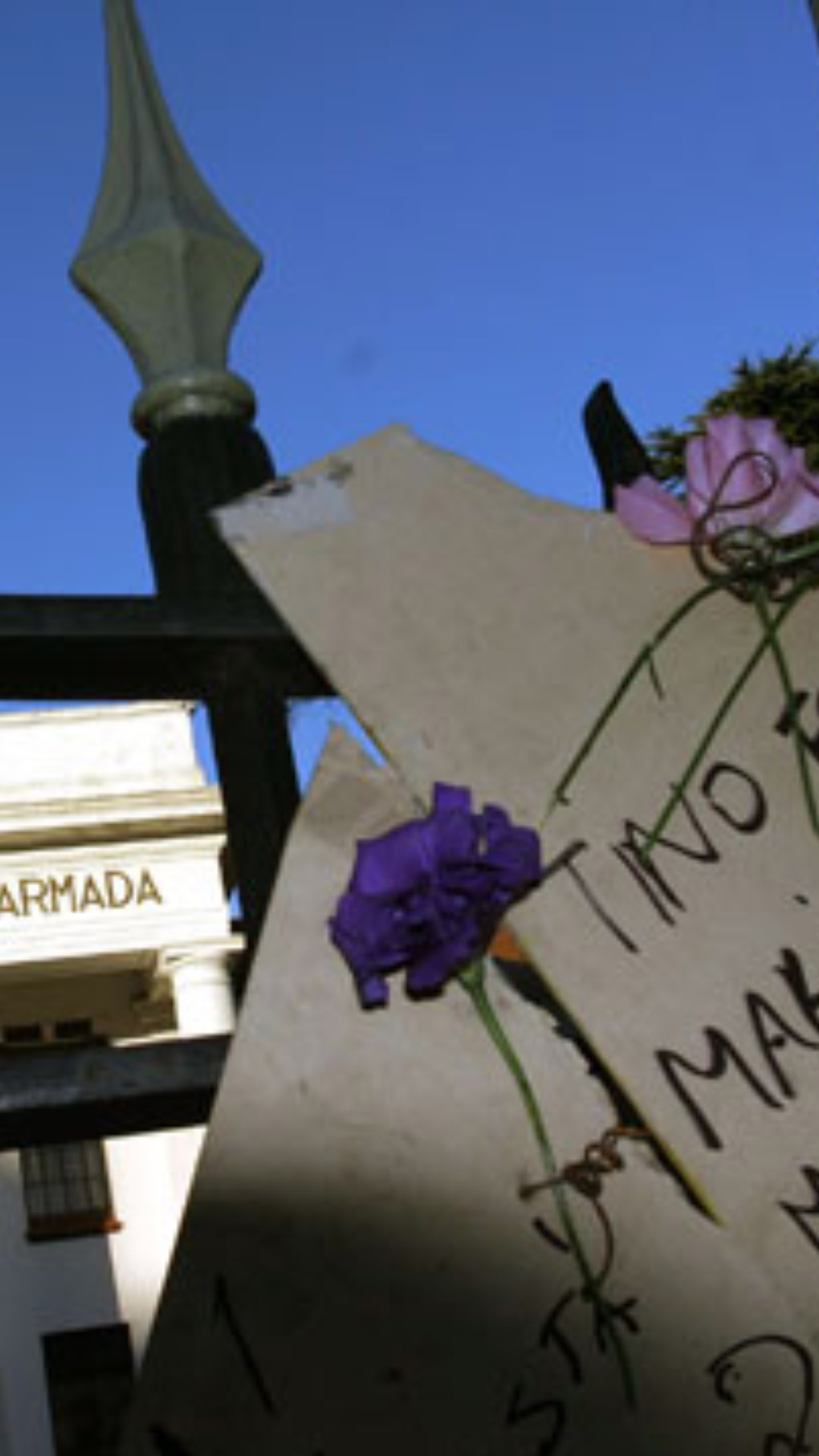 Portada de la Escuela de Mecánica de la Armada, en la reja hay colgadas flores y un cartel con los nombres Tino Fontenla, Marito Galarza, Maria Elena Garaza, Emilio Gonzalez.