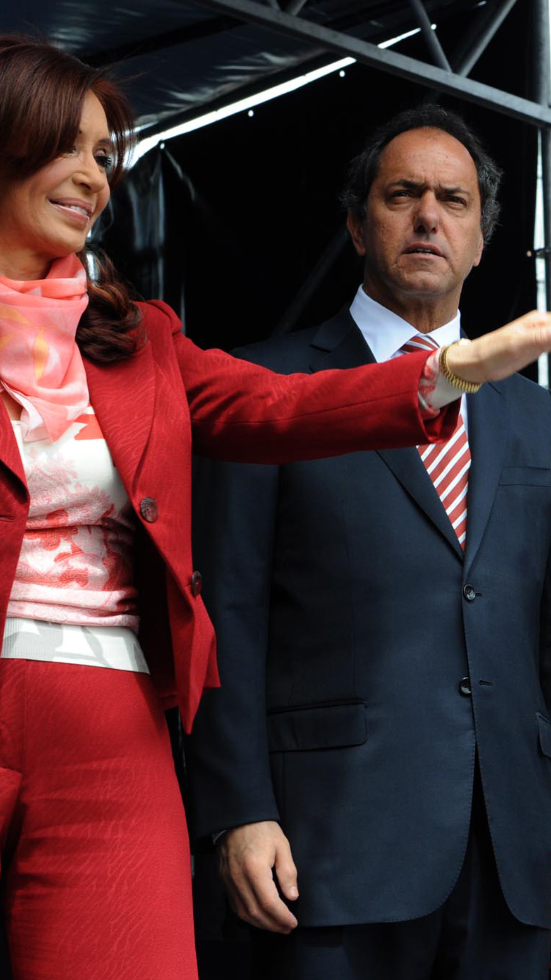 Portada de acto de inauguración de la Universidad Nacional de José C. Paz. La foto es exterior, de día y muestra en un plano conjunto a la entonces Presidenta de la República Argentina,  Cristina Fernandez de Kirchner saludando al público. También integra la imagen el gobernador de la provincia de Buenos Aires de esa época, Daniel Scioli; el intendente de ese momento de la Municipalidad de José C. Paz,  Mario Ishi quien está hablando con  Nestor Kirchner (diputado por la provincia de Buenos Aires en esos años) y este le señala algo que no figura en la escena de la foto. Todos ellos están con gestos felices en un escenario mirando al público que está fuera de la escena fotográfica (fuera de campo).